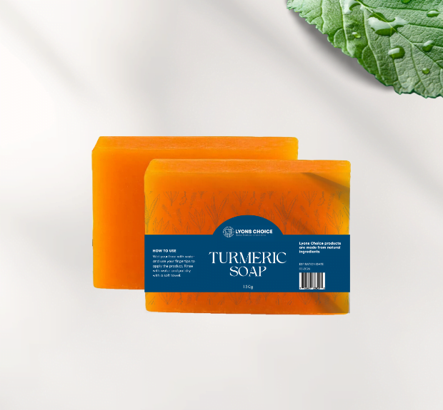 This is an image of turmeric sopa - a product listed on page Wholesale - Lyons Choice woocommerce store. The image features a packaging of soap with turmeric yellow color of cuboidal packing and the name of the product written on blue color background and two pieces of fresh turmeric the green leaves also featuring on the left side of the product.